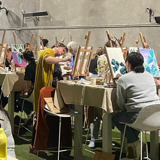 Group of people painting at tables with art supplies in a studio setting creating in a painting workshops