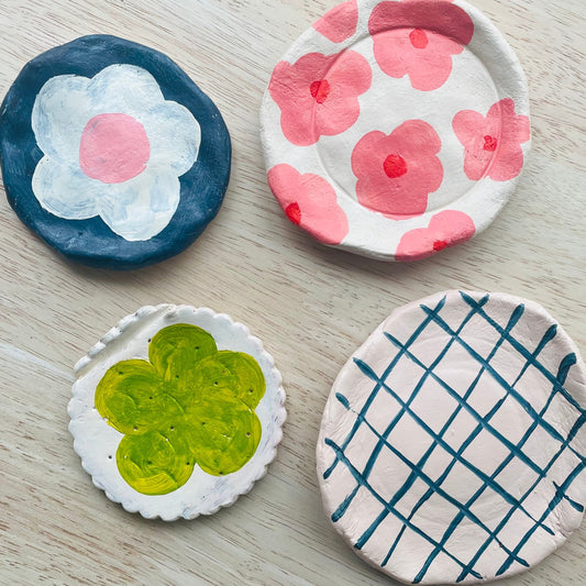 Four clay coasters with floral, grid, and clover designs on a wooden surface.