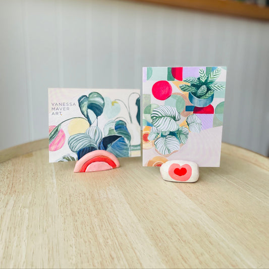 Colourful greeting cards on a wooden surface shown in handmade clay photo stands painted pink, red and cream with a blurred background