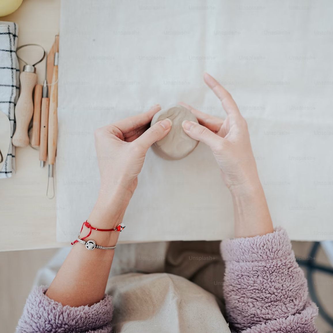 Person holding a white clay with tools on a wooden surface