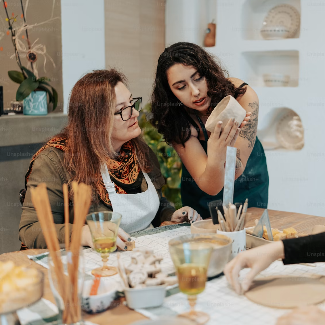 Two women creating clay objects. One woman instructs the other on the next steps